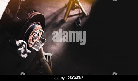 Freno a disco per auto e pinza senza ruota su cavalletto nel garage auto riparazione , banner panoramico con spazio copia su sfondo nero Foto Stock