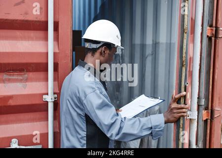 Vista posteriore del lavoratore che indossa l'hardHat mentre controlla i contenitori al molo di spedizione, spazio per le copie Foto Stock