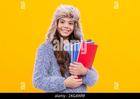 bambino allegro in maglione e cappello con libro da lavoro su sfondo giallo, istruzione Foto Stock