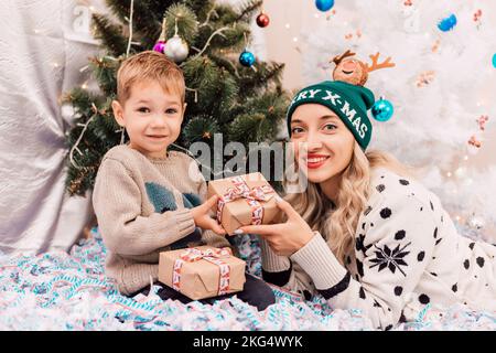 Madre e figlio scambiano regali vicino all'albero di Natale. Regali di Natale Foto Stock