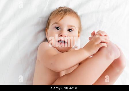 felice bambino steso su un lenzuolo bianco e tenendo i piedi Foto Stock