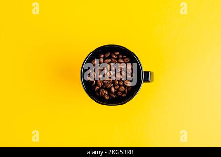 Chicchi di caffè in una tazza nera su sfondo giallo Foto Stock
