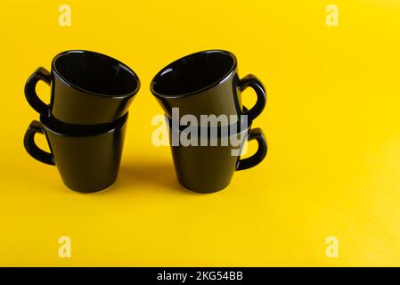Quattro tazze di caffè nere su sfondo giallo Foto Stock