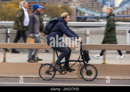 Una donna che si collega durante l'ora di punta su una bicicletta elettrica pieghevole Brompton attraverso London Bridge, Londra, Regno Unito. 18 Nov 2022 Foto Stock