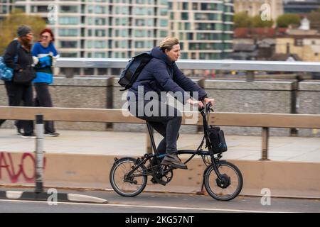 Una donna che si collega durante l'ora di punta su una bicicletta elettrica pieghevole Brompton attraverso London Bridge, Londra, Regno Unito. 18 Nov 2022 Foto Stock