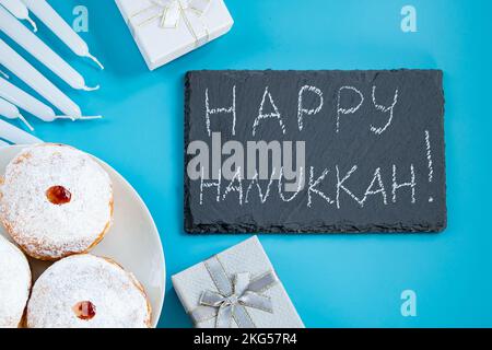 Felice Hanukkah. Dessert ebraico sufganiyot ciambelle su sfondo blu. Simbolo di festa religiosa giudaismo. Iscrizione sul bordo del gesso. Foto Stock