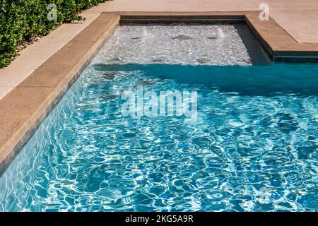 Una nuova piscina rettangolare con bordi in cemento marrone chiaro nel cortile recintato di una nuova casa di costruzione Foto Stock