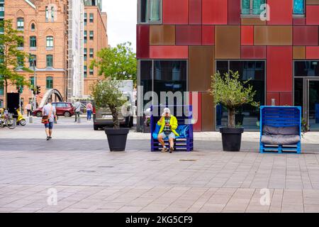 Un uomo seduto su un sedile a Überseequartier a HafenCity ad Amburgo. E' stato progettato come il quartiere centrale del quartiere. Foto Stock