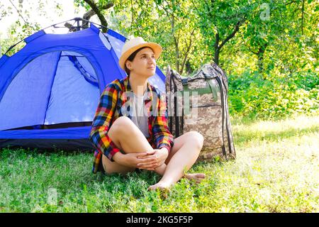 Defocus giovane donna seduta vicino campeggio tenda all'aperto circondata da una bella natura. Freelance, sabbatico, salute mentale. Riposo. Campo estivo. Sogno. Foto Stock