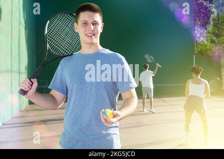 Sorridente giovane frontenis in piedi sul campo di frontone all'aperto Foto Stock