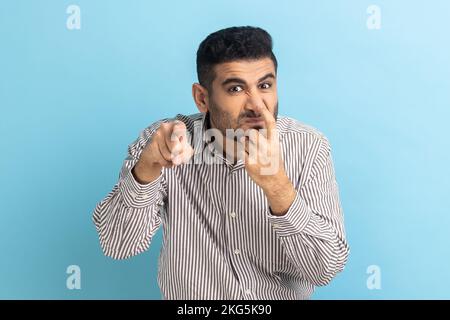 Sei bugiardo. Ritratto dell'uomo arrabbiato che tocca il naso con un dito e mostra un gesto di menzogna, linguaggio del corpo, indossando una camicia a strisce. Studio in interni isolato su sfondo blu. Foto Stock