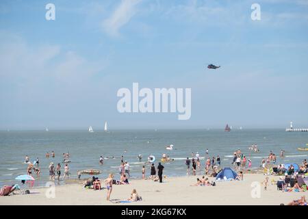 Un elicottero Sea King dipinto con i colori della bandiera belga sull'acqua con persone che si rilassano sulla spiaggia Foto Stock