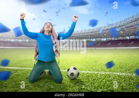 L'uomo asiatico con keffiyeh festeggia la vittoria con espressioni eccitate nello stadio di calcio Foto Stock