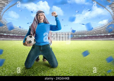 L'uomo asiatico con keffiyeh festeggia la vittoria con espressioni eccitate nello stadio di calcio Foto Stock