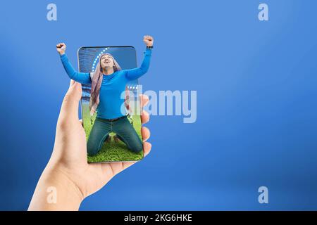 L'uomo asiatico con keffiyeh festeggia la vittoria con espressioni eccitate sullo stadio di calcio sullo schermo del telefono cellulare Foto Stock