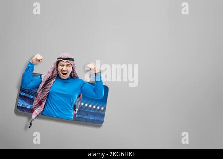 L'uomo asiatico con keffiyeh festeggia la vittoria con espressioni eccitate sullo stadio di calcio sullo schermo del telefono cellulare Foto Stock