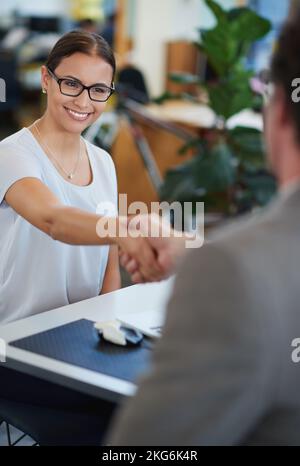 Ti meriti questa promozione. un paio di colleghi che scuotono le mani mentre sono seduti in ufficio. Foto Stock