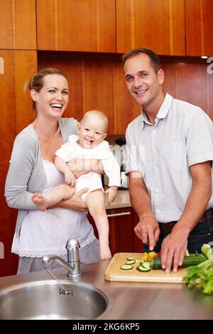 Divertimento per tutta la famiglia in cucina. Un ritratto di una coppia felice che tiene il loro bambino mentre sta in piedi nella cucina. Foto Stock