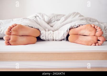 Condivisione di un letto. un paio di piedi che si scopano sotto un piumino. Foto Stock