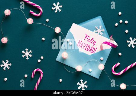 Feliz Navidad significa buon Natale in lingua spagnola. Biglietto d'auguri nella busta di carta. Sfondo di Natale su carta verde con canne di caramelle magenta Foto Stock