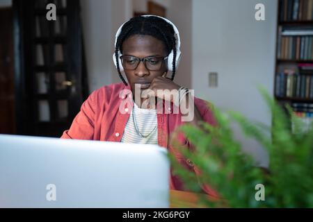 Concentrato di successo afro-americano uomo SVILUPPATORE IT in cuffie è lavora si siede alla scrivania con notebook Foto Stock