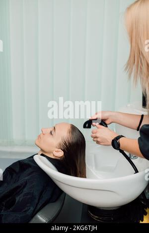 Il parrucchiere lava i capelli del cliente nel salone. Tintura e taglio dei capelli Foto Stock