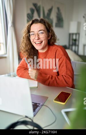 Felice giovane studentessa che ride usando un notebook seduto alla scrivania che studia online. Foto Stock