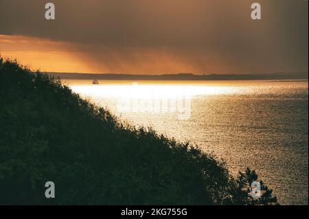 Sulla costa di Hundested. I raggi del sole che si infrangono attraverso il suggestivo cielo attraverso le nuvole al tramonto. Montagna con alberi in primo piano. Paesaggio s Foto Stock