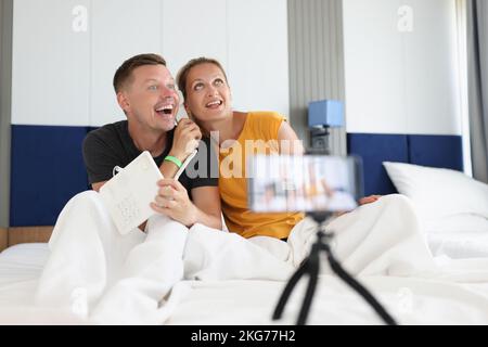 Felice coppia sorridente che registra video a letto sullo smartphone Foto Stock