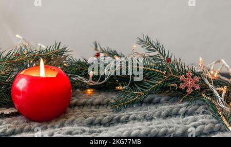 Composizione natalizia con candela, elemento a maglia con rami di abete. Foto Stock