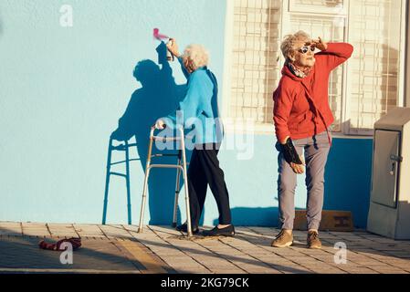 Donne anziane, amici e vernice spray per vandalismo, graffiti e Street art disegno sul muro casa di cura edificio. Gli anziani pazzi infrangono la legge Foto Stock