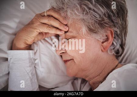 Sonno, mal di testa e donna anziana in un letto con stress, ansia e stanco. Malato, triste e di fronte ad una donna anziana che sogna di depressione e di sonno Foto Stock