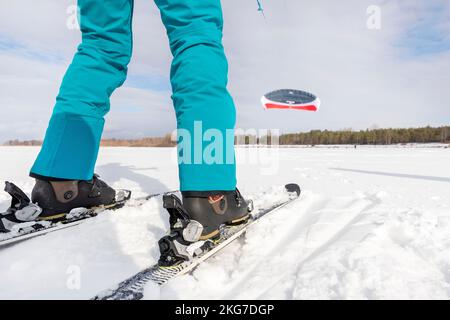 Vista dal basso del kitesurf Rider Godetevi il kite surf board in tuta calda nella luminosa giornata invernale di sole sul lago ghiacciato superficie innevata. Sport invernale Foto Stock