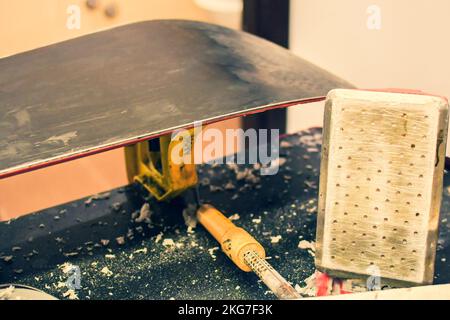 L'operaio del negozio di riparazione sciistico scioglie la cera rossa sulle tavole da snowboard con uno speciale ferro da stiro. Servizio di scialinatura e preparazione dello snowboard Foto Stock