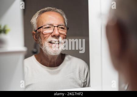 L'uomo anziano sta guardando il viso in bagno e sta pensando di radere la barba. Foto Stock