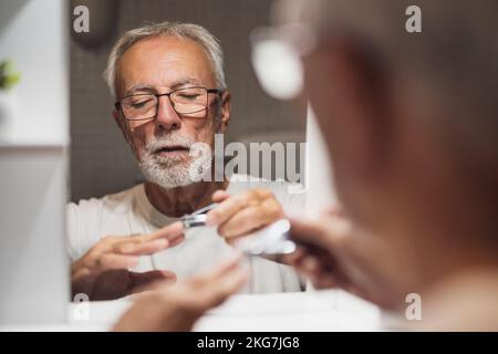 L'uomo anziano sta tagliando le unghie in bagno. Foto Stock