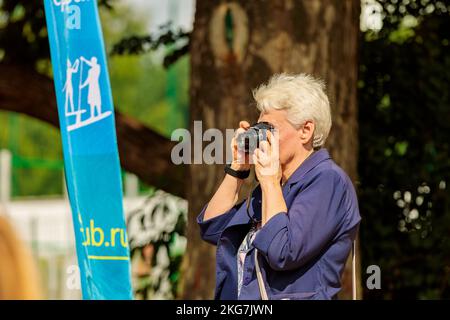 Una donna adulta fotografa la gente sulla spiaggia in estate. Evento di paddleboarding. Russia Zelenograd 14 agosto 2021 Foto Stock