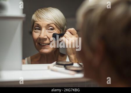La donna matura sta applicando il blush nella stanza da bagno. Foto Stock