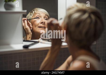 La donna matura sta applicando il mascara nella stanza da bagno. Foto Stock
