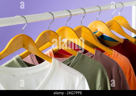 Magliette colorate esposte sul corrimano dell'abbigliamento e spazio copia su sfondo viola Foto Stock