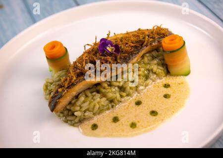 Ricetta per filetto di branzino fritto con risotto alle erbe, salsa al vino bianco, crema fresca, rotolo di carota e strisce di zucchine Foto Stock