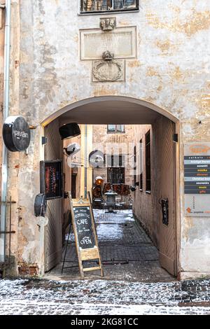Ingresso con cartello di un accogliente caffè nel centro storico di riga, in Lettonia, in inverno con tavoli e sedie coperti di neve e riflettori vintage, verticale Foto Stock