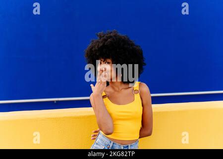 Bella giovane donna africana felice con capelli ricci afro passeggiando in città - allegro ritratto studente nero su sfondo colorato parete Foto Stock