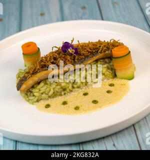 Ricetta per filetto di branzino fritto con risotto alle erbe, salsa al vino bianco, crema fresca, rotolo di carota e strisce di zucchine Foto Stock