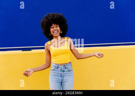 Bella giovane donna africana felice con capelli ricci afro passeggiando in città - allegro ritratto studente nero su sfondo colorato parete Foto Stock