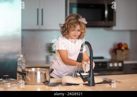 Divertenti ragazzi gemelli che aiutano in cucina con piatti di lavaggio. Bambini che si divertono con i lavori di casa. Un ragazzo carino lavare i piatti vicino al lavandino in cucina. Foto Stock