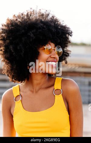 Bella giovane donna africana felice con afro ricci acconciatura passeggiare in città - allegro nero studente ritratto all'aperto Foto Stock