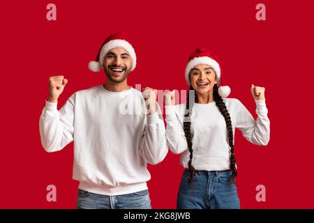 Ritratto di coppia araba overjoyed che indossa i cappelli di Santa celebrare insieme il successo Foto Stock