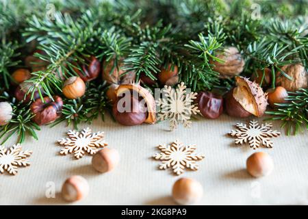 Rami verdi con noci sparse su rami di abete e fiocchi di neve in legno giacciono su carta artigianale Foto Stock