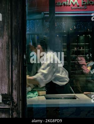 Una lavoratrice in un ristorante a Soho, Londra, che eseguiva un'attività, fotografata attraverso una finestra con condensa. Foto Stock